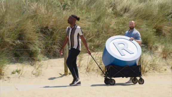 Mannen verplaatsen groot r-teken op het strand