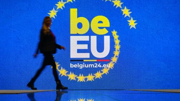 Persoon loopt naast logo België voorzitter van de EU 